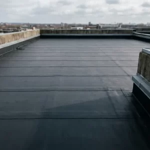 Plat commercieel dak met donkere bitumineuze dakbedekking, parallelle naadstroken en metalen randafwerking op lage borstwering.