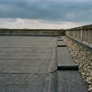 Commercieel plat dak met vers aangebrachte bitumen dakbedekking, zorgvuldig afgewerkte naden en grindrand onder bewolkte lucht.