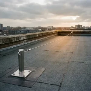 Plat commercieel dak met bitumineuze dakbedekking, roestvrijstalen verankeringsanker en gespannen veiligheidslijn onder bewolkte Nederlandse lucht.