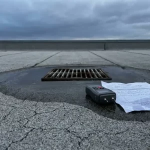 Verweerde EPDM-dakbedekking met scheurvorming en waterophoping bij afvoer, vochtmeter en inspectierapport op plat commercieel dak.