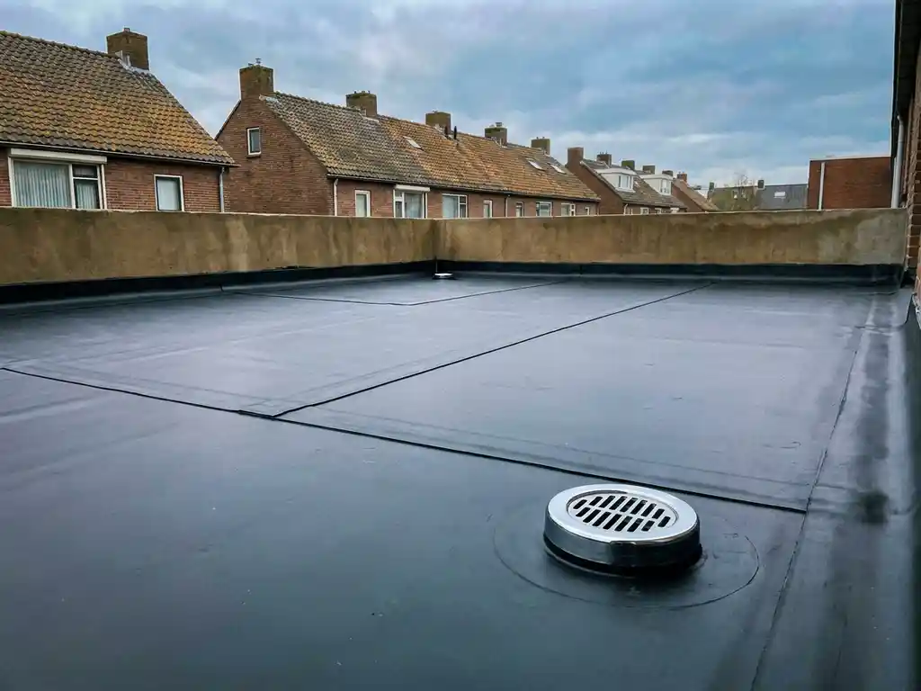 Nieuw aangelegd EPDM dakmembraan met afgewerkte naden en chromen afvoerput op een plat dak in Nederlandse buitenwijk.