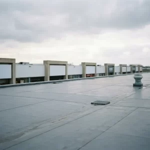 Groot plat commercieel dak met grijze EPDM-membraan, afvoerputten en ventilatieopeningen, winkelgevels zichtbaar op straatniveau.