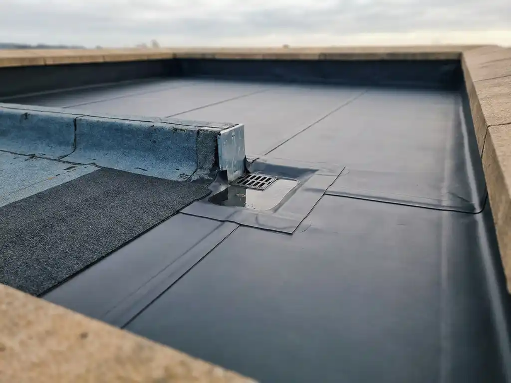Bovenaanzicht van een plat dak met EPDM-membraan, nette naden, dakafvoer en vers aangebracht dakdichtingsfolie naast verouderd materiaal.