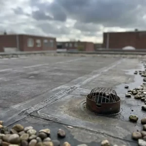 Verweerd EPDM-dakbedekking op een plat commercieel dak in Nederland, met naadlijnen, afvoerput en grindrand onder bewolkte lucht.