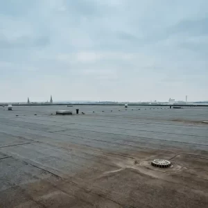 Uitgestrekt EPDM-dakoppervlak van een commercieel gebouw met zichtbare naden en afvoerpunten onder bewolkte Nederlandse lucht.