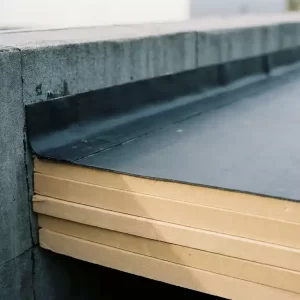 Dakranddetail met gelaagde isolatiepanelen onder bitumineuze dakbedekking op een commercieel betonnen gebouw.