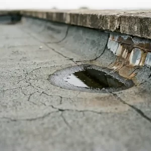 Verweerde platte dakmembraan met oppervlaktescheuren, wateropstapeling en zichtbaar dakranddetail bij een borstwering.