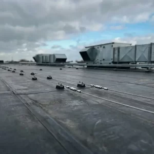 Veiligheidankers en roestvrijstalen lijnkabels op een commercieel EPDM-dak met industriële ventilatieunits op de achtergrond.